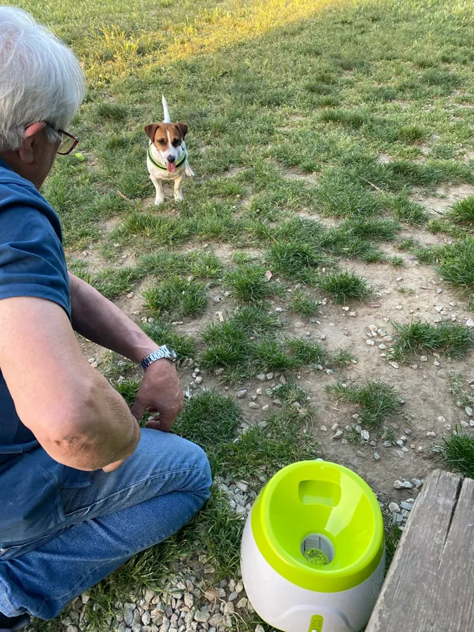 Un homme accroupi dans un jardin avec son jack russell et le lanceur